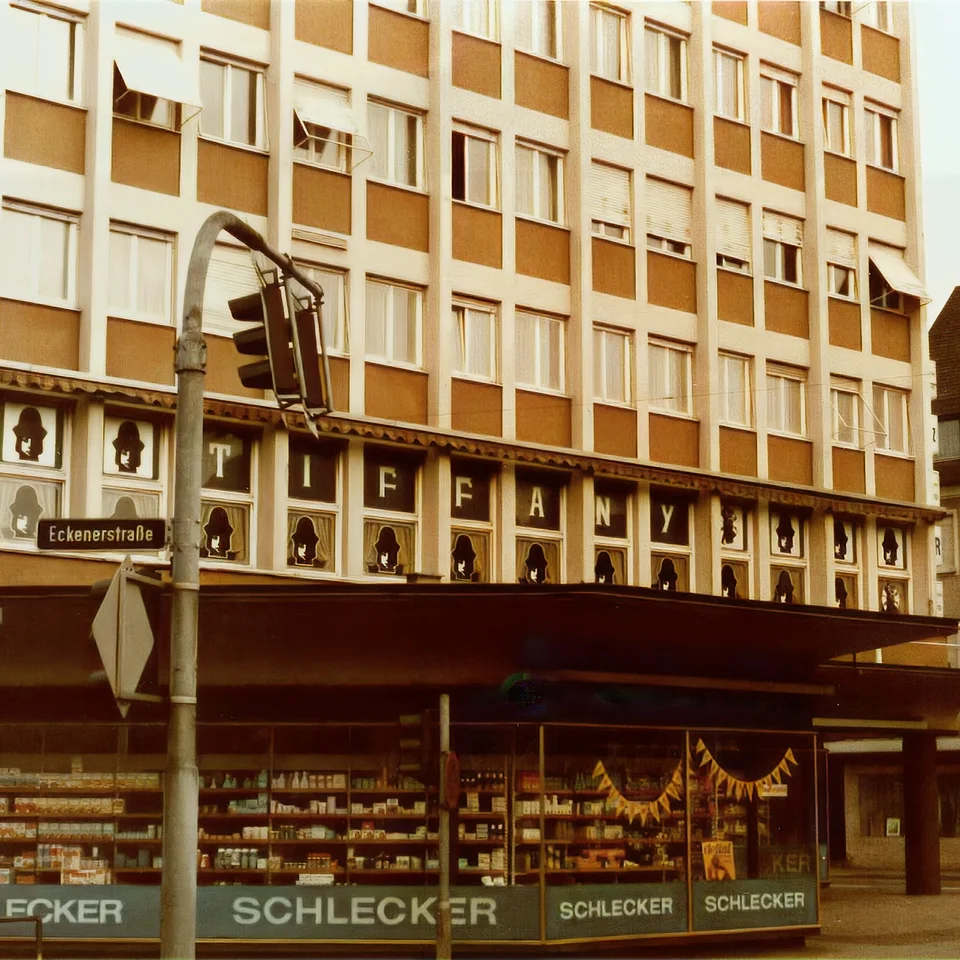 Mehrstöckiges Geschäftsgebäude mit dem Schriftzug SCHLECKER auf der unteren Ebene, davor Straßenkreuzung mit Ampel und Straßenschild Eckenerstraße.