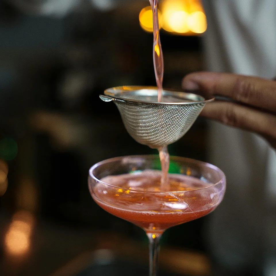 Cocktail wird durch ein Sieb in ein Cocktailglas mit Eiswürfeln eingegossen.