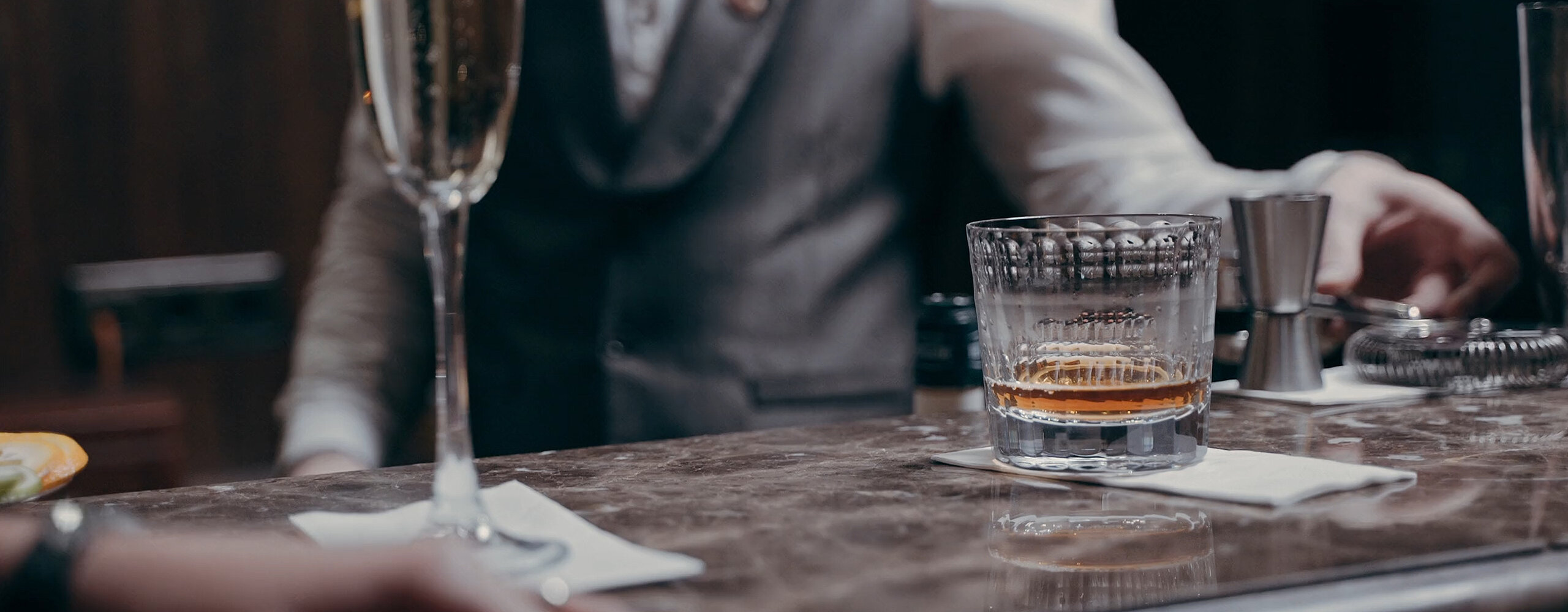 Ein Barkeeper hinter einer Bar mit einem Glas Whiskey und einem Glas Sekt auf der Marmorarbeitsfläche.
